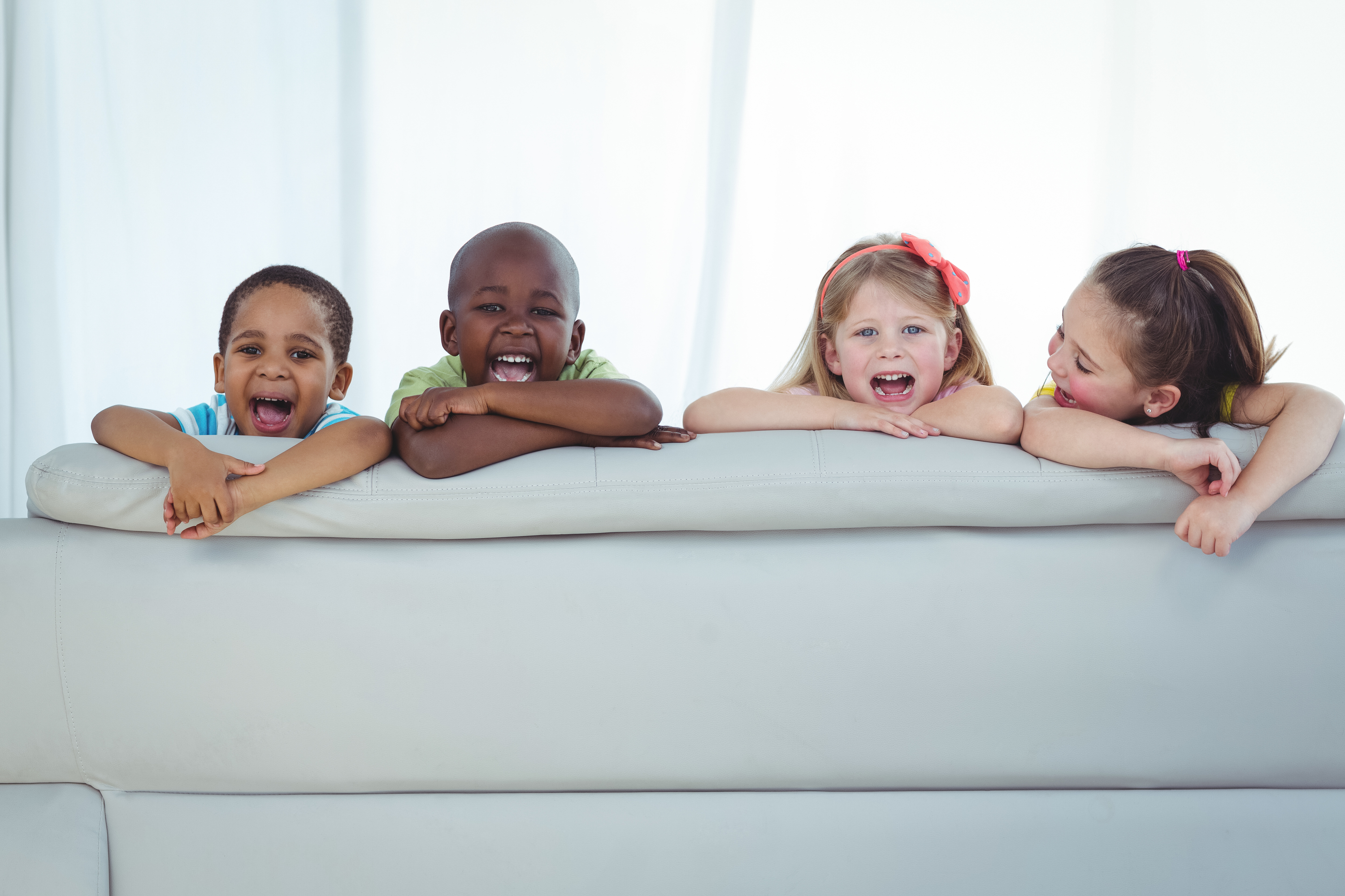 Happy kids looking from the back of the couch and smiling